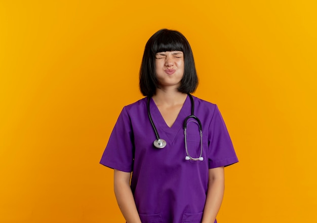 Foto gratuita infastidito giovane dottoressa bruna in uniforme con lo stetoscopio che soffia sulle guance con gli occhi chiusi