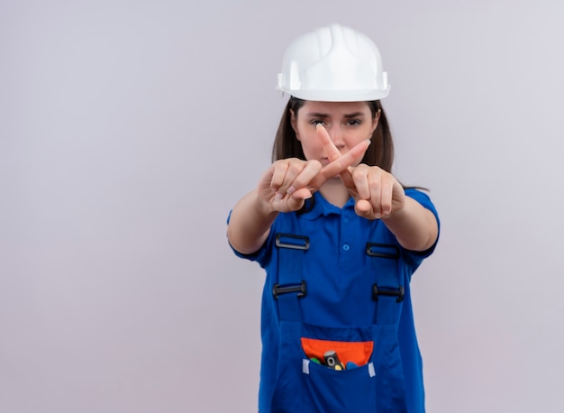 Ragazza infastidita giovane costruttore con casco di sicurezza bianco e gesti uniformi blu no con le dita su sfondo bianco isolato con spazio di copia