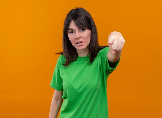 緑のシャツを着たイライラした若い白人の女の子は、孤立したオレンジ色の背景を前に指します