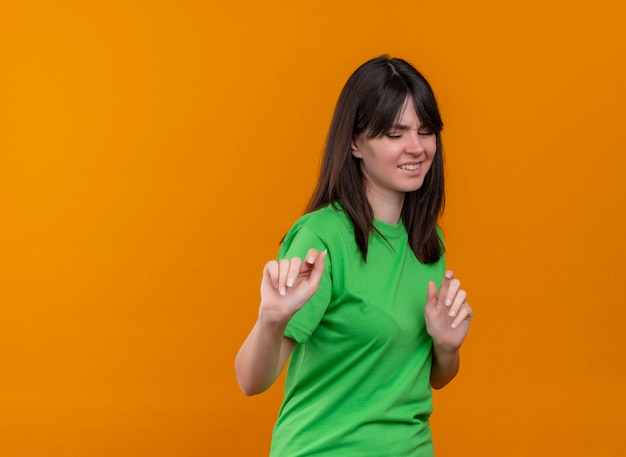 緑のシャツを着たイライラした若い白人の女の子は、コピースペースで孤立したオレンジ色の背景に何かを押すふりをします
