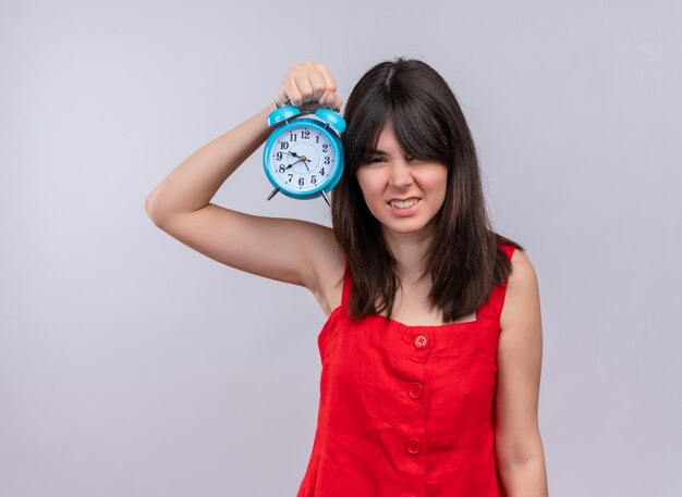 Annoyed young caucasian girl holding clock with hand down on isolated white background with copy space