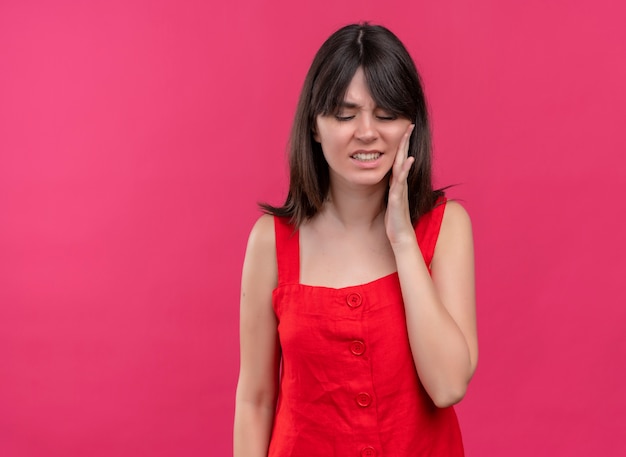 Annoyed young caucasian girl puts hand on face and looks down on isolated pink background with copy space