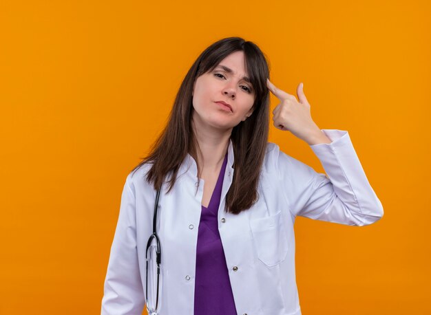 Annoyed young female doctor in medical robe with stethoscope gestures headshot with hand on isolated orange background with copy space