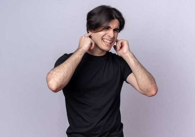 Annoyed young handsome guy wearing black t-shirt closing ears isolated on white wall