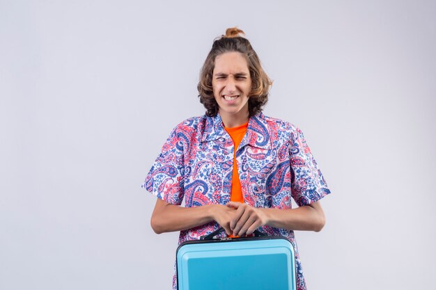 Annoyed young handsome traveler guy holding suitcase unhappy and frustrated with something keeping eyes closed standing 