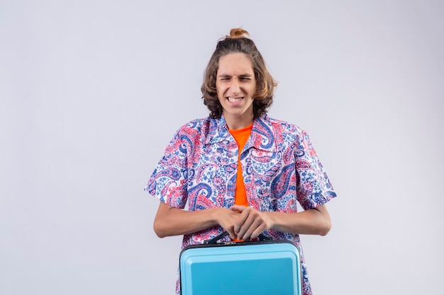 Annoyed young handsome traveler guy holding suitcase unhappy and frustrated with something keeping eyes closed standing 