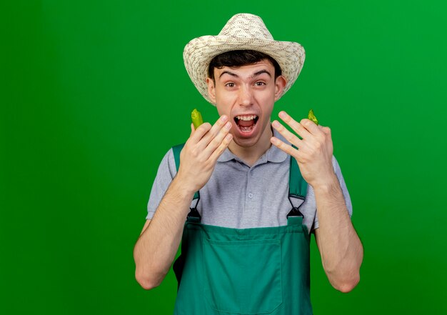 Foto gratuita il giovane giardiniere maschio infastidito che porta il cappello di giardinaggio tiene il peperoncino