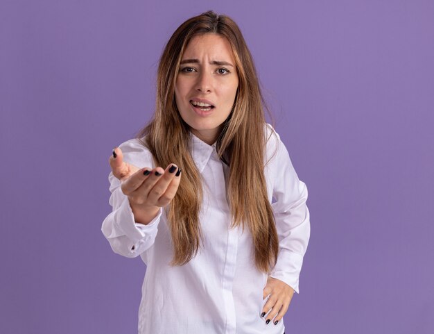 Annoyed young pretty caucasian girl looks and points with hand isolated on purple wall with copy space