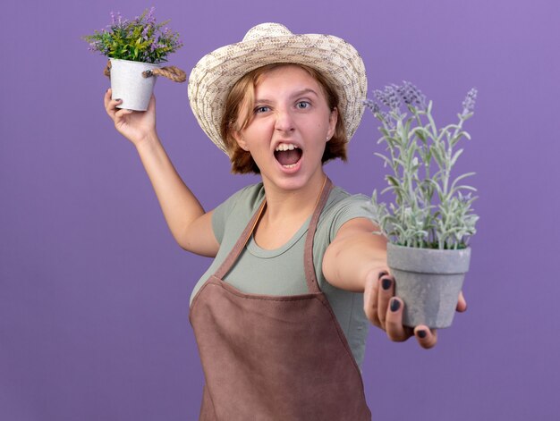 植木鉢に花を保持しているガーデニング帽子をかぶってイライラする若いスラブの女性の庭師