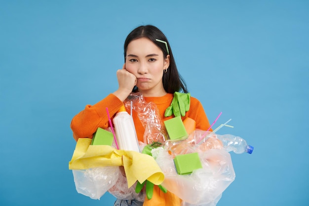 無料写真 リサイクルのためにプラスチックのゴミを持って家の掃除をしているイライラした若い女性は、廃棄物の収集にうんざりしています