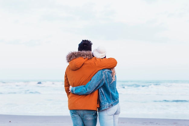 Anonymous couple in warm clothes on beach