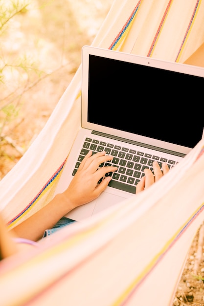 Free photo anonymous female lying in hammock and typing on laptop