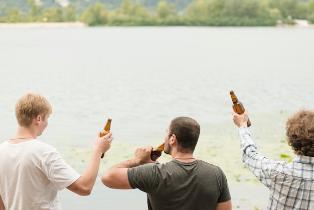 Free photo anonymous friends enjoying beer near water