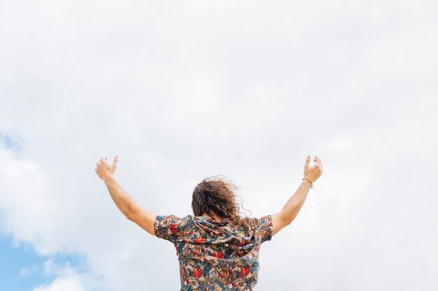 Anonymous male rising hands to cloudy sky