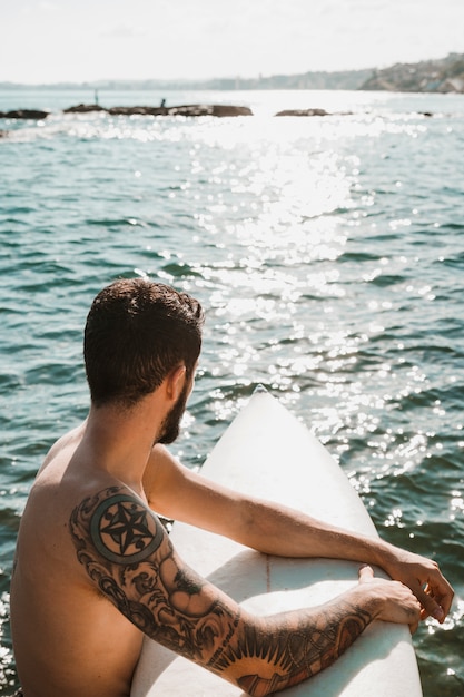 Free photo anonymous man floating on surfboard