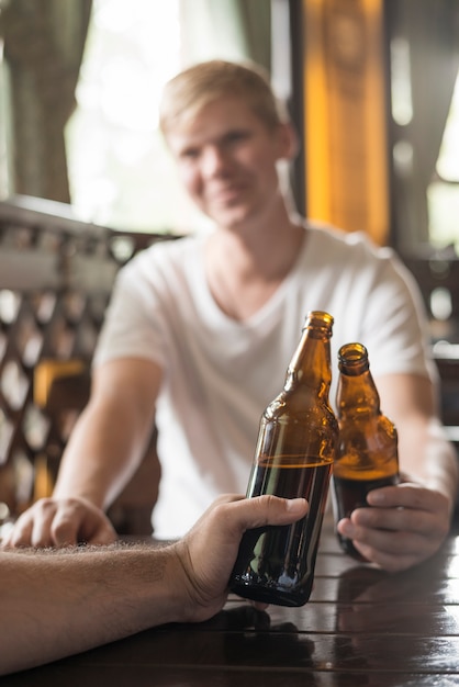 Anonymous men clinking bottles at pub table