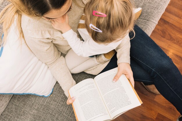 Anonymous mother and daughter reading on couch