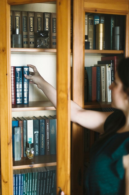 Free photo anonymous woman taking book from bookshelf