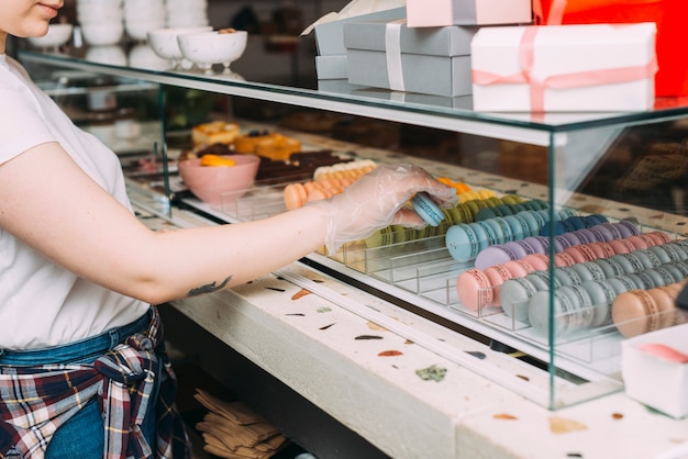 Free photo anonymous woman taking macaroons from display case