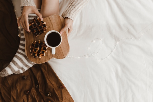 Anonymous woman with drink and waffles on bed