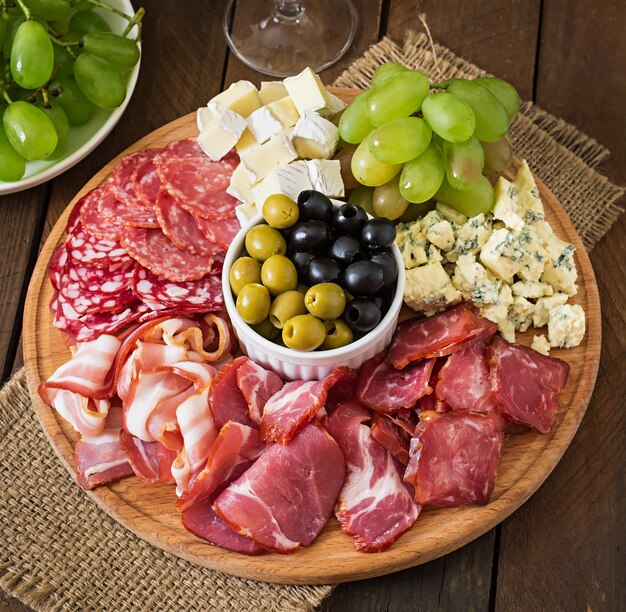 ベーコン、ジャーキー、サラミ、チーズ、木製のテーブルのブドウの盛り合わせ前菜