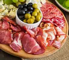 Foto gratuita piatto di antipasto con pancetta, scatti, salame, formaggio e uva su un tavolo di legno