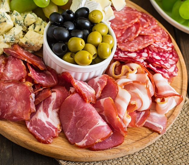 Antipasto catering platter with bacon, jerky, salami, cheese and grapes on a wooden table