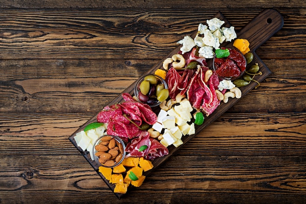 Antipasto catering platter with bacon, jerky, sausage, blue cheese and grapes on a wooden table. Top view