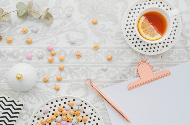 Antique pen on clipboard with candies and ginger lemon tea cup on tablecloth