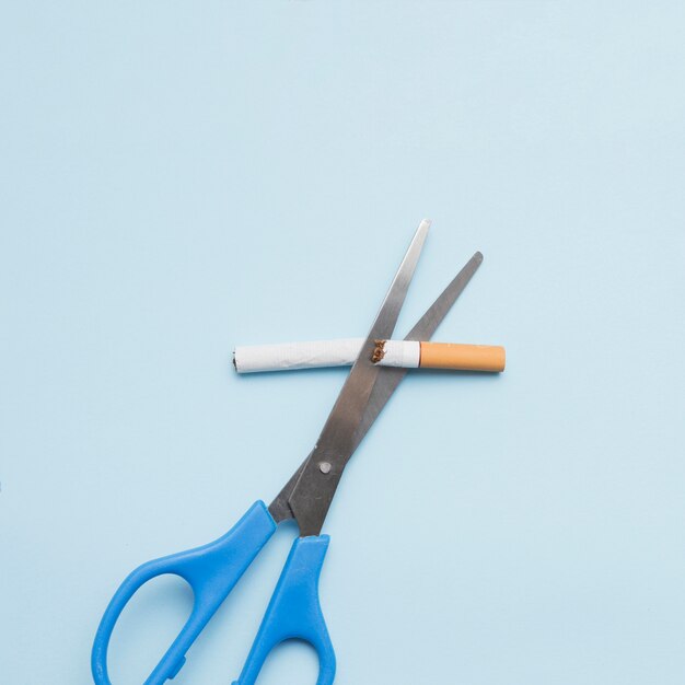 Antismoking concept with cigarette and scissor on colored backdrop