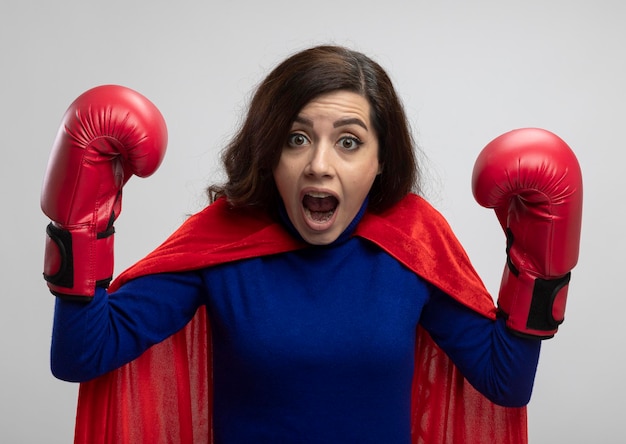 Anxious caucasian superhero girl with red cape wearing wearing boxing gloves stands