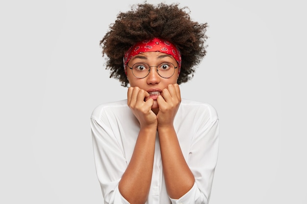 Free photo anxious dark skinned woman bites finger nails nervously, feels embarrassed in difficult life situation