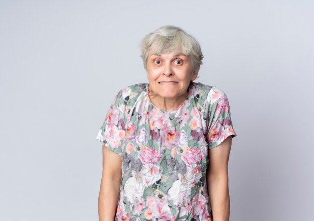 Anxious elderly woman stands isolated on white wall