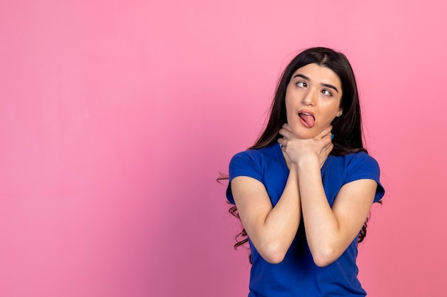 Anxious girl trying to choke herself on pink background