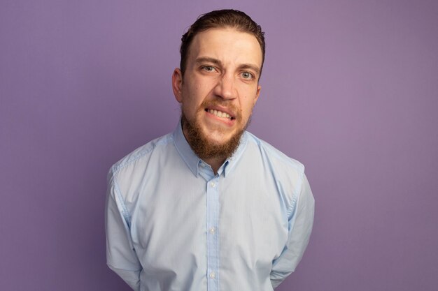 Anxious handsome blonde man bites lips isolated on purple wall