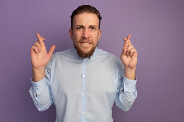 Free photo anxious handsome blonde man crossing fingers isolated on purple wall