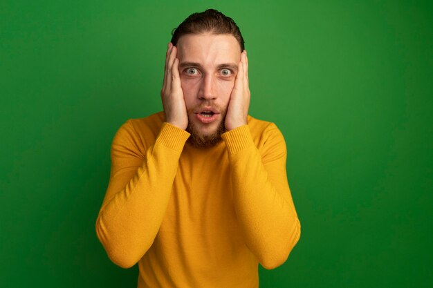 Anxious handsome blonde man puts hands on face on green