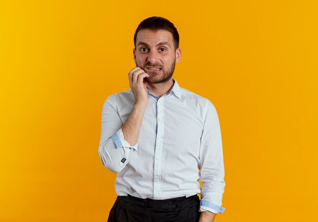 Anxious handsome man bites lips puts hand on chin looking isolated on orange wall