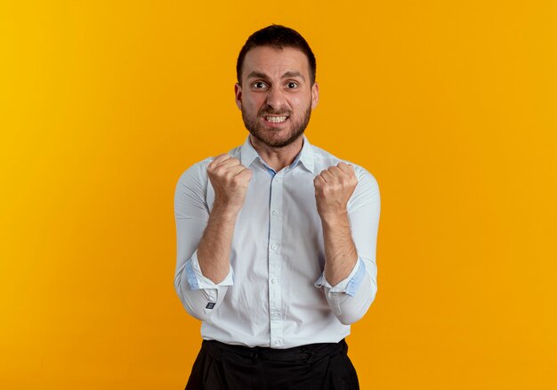 Anxious handsome man keeps fists isolated on orange wall