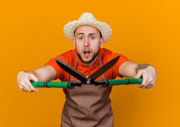 Anxious male gardener wearing gardening hat holds garden clippers 