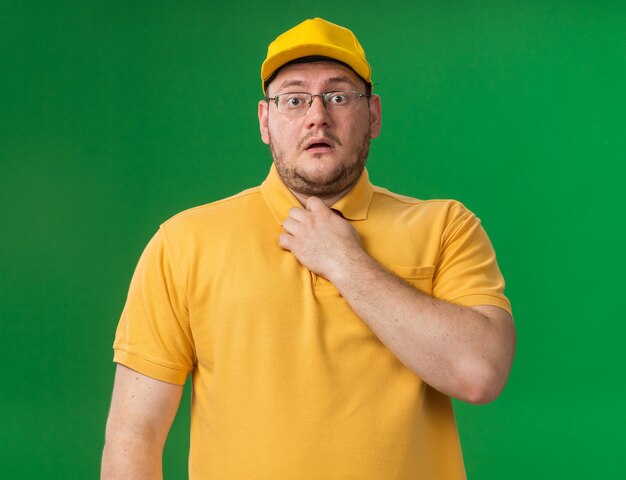 anxious overweight young deliveryman in optical glasses holding collar  isolated on green wall with copy space