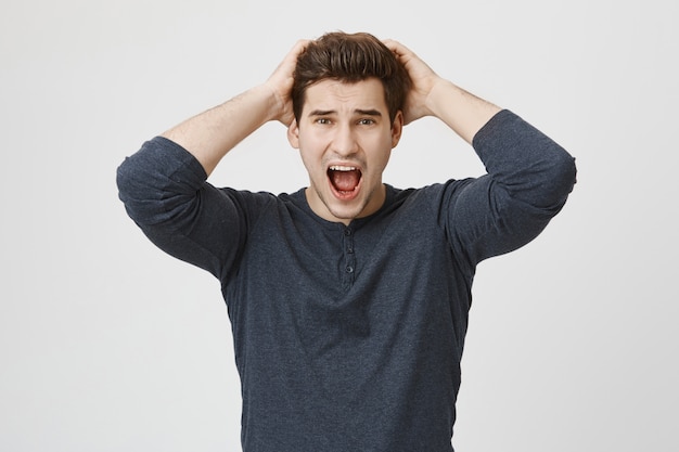 Anxious panicking handsome man shouting alarmed, grab head