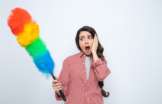 Anxious pretty caucasian cleaner woman holding feather duster and putting hand o her face