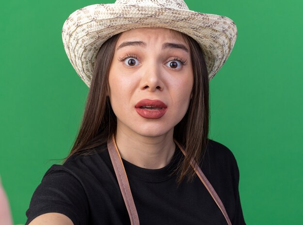 Anxious pretty caucasian female gardener wearing gardening hat looking at camera on green