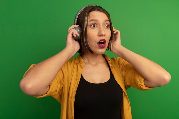 Anxious pretty caucasian woman on headphones looks at side on green