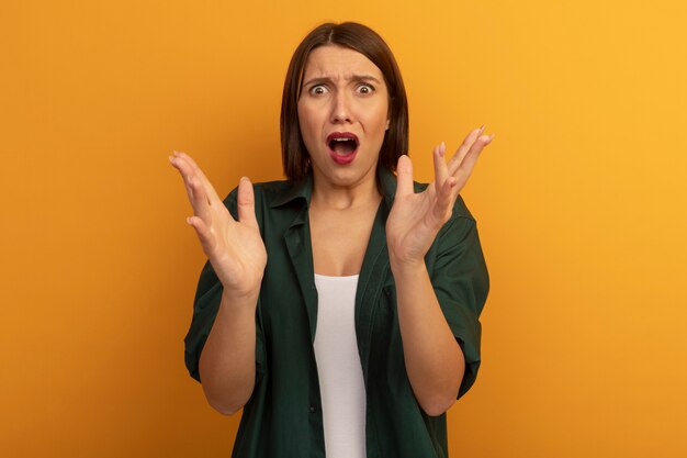 Anxious pretty caucasian woman holds hands open on orange