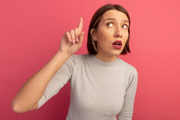 Anxious pretty caucasian woman looks and points up isolated