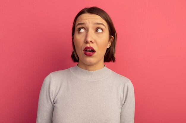 Anxious pretty caucasian woman looks at side on pink