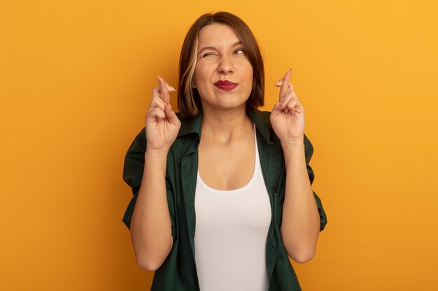 Anxious pretty caucasian woman stands with crossed fingers on orange