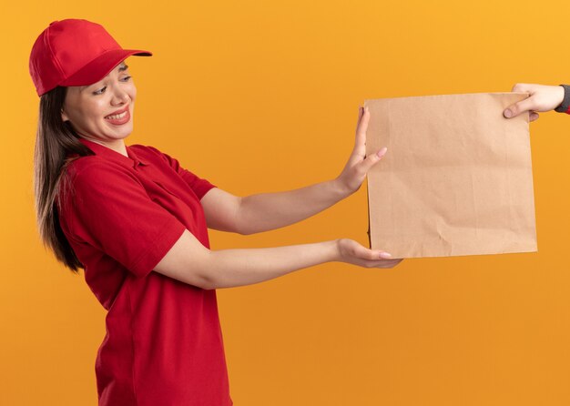 Anxious pretty delivery woman in uniform gives paper package to someone